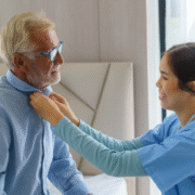 Caregiver assisting elderly man button his shirt.