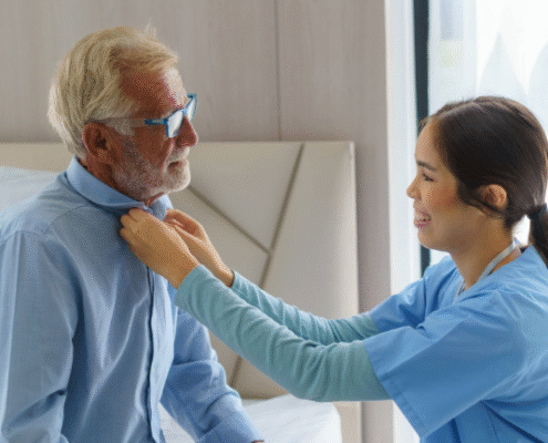 Caregiver assisting elderly man button his shirt.