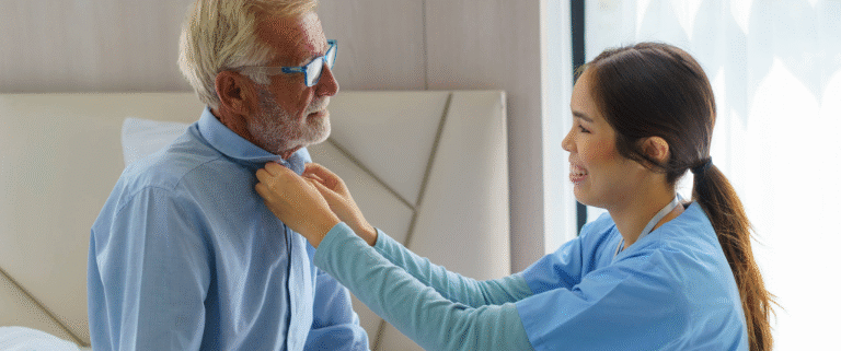 Caregiver assisting elderly man button his shirt.